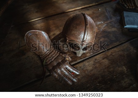 Medieval helmet and glove on a wood table. Armor of middle-ages, knightly equipment, armory forge. Vanitas still life.