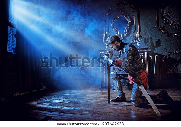 Medieval knight in armor makes an oath of allegiance by kneeling and bowing his head on the sword in the castle before the battle.