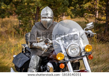 A medieval knight in chain mail and a helmet sits on a motorcycle. A trip through the woods.