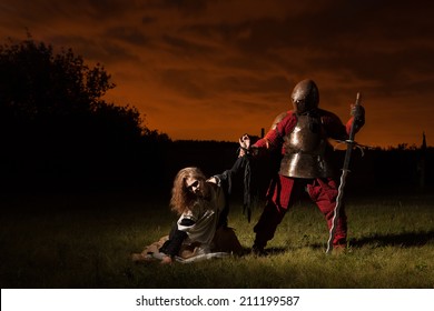 Medieval Knight Is Going To Make An Execution Of A Witch. Night Forest On The Background.