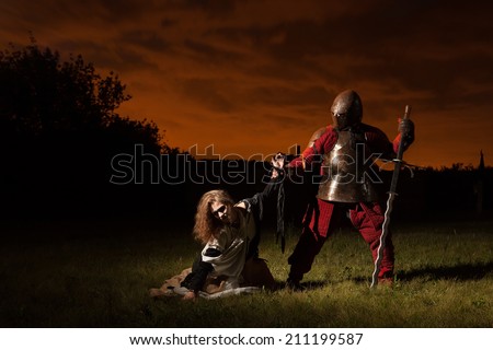 Medieval knight is going to make an execution of a witch. Night forest on the background.