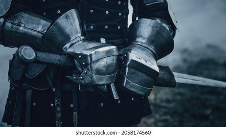 Medieval Knight Wearing Armour And Helmet, Draws Sword From Shearh, Ready To Fight, Kill His Enemy In Battle. Warrior Soldier On Battlefield. War, Invasion, Crusade. Cinematic Historic Reenactment