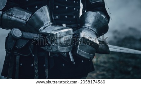 Medieval Knight Wearing Armour and Helmet, Draws Sword from Shearh, Ready to Fight, Kill His Enemy in Battle. Warrior Soldier on Battlefield. War, Invasion, Crusade. Cinematic Historic Reenactment