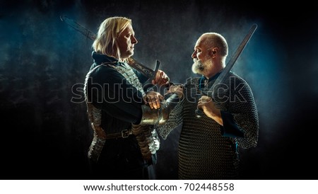 Medieval knights are crossing their hands in the brotherhood of War. Dark background.