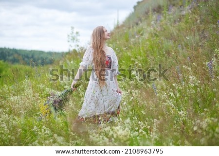 Medieval lady in historical dress. Aroma of spring nature, wild flowers, blue sky, sunshine.
Beautiful happy tender young woman enjoying the smell of summer wildflowers.