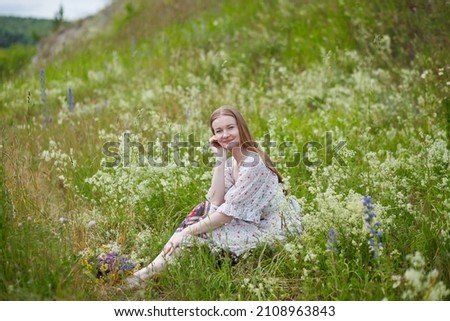 Medieval lady in historical dress. Aroma of spring nature, wild flowers, blue sky, sunshine.
Beautiful happy tender young woman enjoying the smell of summer wildflowers.