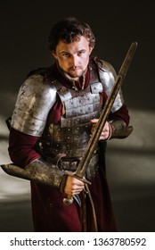 Medieval Man Knight In Armor And Weapon On Dark Background. Portrait Of The Knight