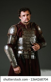 Medieval Man Knight In Armor And Weapon On Dark Background. Portrait Of The Knight