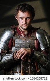 Medieval Man Knight In Armor And Weapon On Dark Background. Portrait Of The Knight