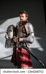 Medieval Man Knight In Armor And Weapon On Dark Background. Portrait Of The Knight