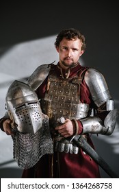 Medieval Man Knight In Armor And Weapon On Dark Background. Portrait Of The Knight