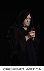 Medieval Monk In Hooded Robe Holding Crucifix And Looking At Camera Isolated On Black