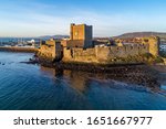 Medieval Norman Castle in Carrickfergus near Belfast in sunrise light. Aerial view with marina, yachts,  breakwater, sediments and far view of Belfast in the background