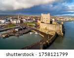 Medieval Norman Castle, harbor with boat ramp and wave breaker in Carrickfergus near Belfast, Northern Ireland, UK. Aerial view in sunset light in winter. Town and stormy clouds in the background