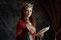 Medieval Queen In Red Dress With Parchment And Crown On Dark Gray Background.