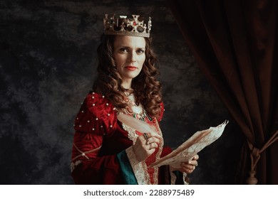medieval queen in red dress with parchment and crown on dark gray background.