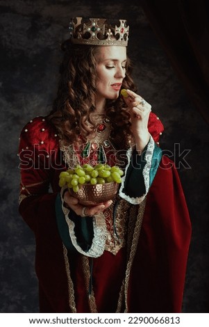 medieval queen in red dress with plate of grapes and crown on dark gray background.