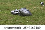 Medieval steel helmet and gauntlets resting on grass, suggesting a historical reenactment or display. The chainmail and detailed armor pieces evoke the imagery of a knight