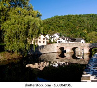 Medieval Village Esch Sur Sure With Classical Houses And Bridge Over Reflection In Sunny Day On Blue Sky Background Outdoors. Diekirch, Luxembourg