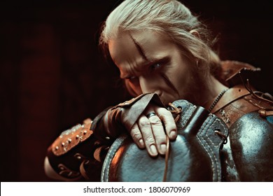 A medieval warrior in armor drinks from a flask by candlelight. Stage portrait. The Witcher man.
