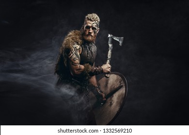 Medieval warrior berserk Viking with tattoo and in skin with axes attacks enemy. Concept historical photo
