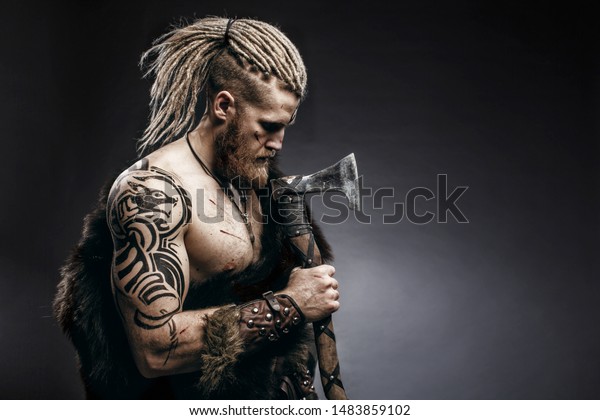 Medieval warrior berserk Viking with tattoo on\
skin, red beard and braids in hair with axe and shield attacks\
enemy. Concept historical\
photo