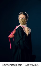 Medieval Young Woman As A Nun In Vintage Clothing And Golden Face Mask With Pink Bra On Dark Blue Background. Concept Of Comparison Of Eras, Fashion, Ad, Healthcare. Royal Person Protected From Covid.