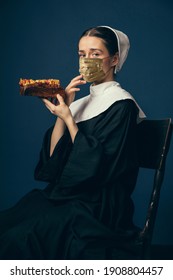 Medieval Young Woman As A Nun In Vintage Clothing And Golden Face Mask With Fast Food On Dark Blue Background. Concept Of Comparison Of Eras, Fashion, Ad, Healthcare. Royal Person Protected From Covid