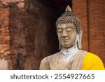 Meditating Buddha stone statue with golden robe at Wat Yai Chai Mongkol on blurred brick background at Ayutthaya, Thailand