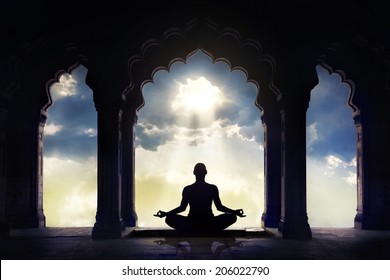 Meditating in old temple with decorative arches at dramatic sunset sky with light hole in the clouds