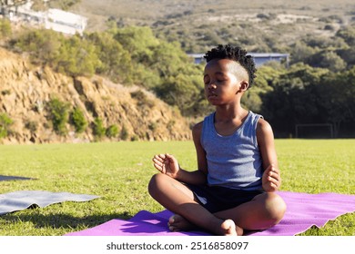 Meditating on yoga mat, african american boy practicing mindfulness outdoors in school setting. Wellness, relaxation, concentration, fitness, exercise, balance - Powered by Shutterstock