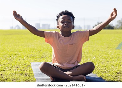 Meditating on yoga mat, african american boy practicing mindfulness outdoors in school setting. Meditation, child, wellness, calm, focus, tranquility - Powered by Shutterstock