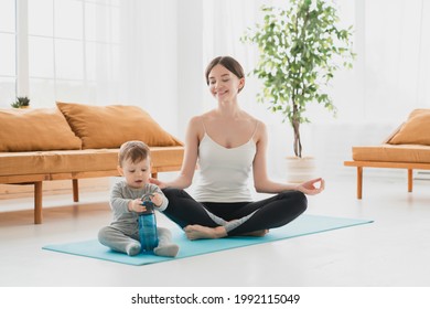Meditating young single mother sitting in lotus yoga position with her little child kid toddler infant trying to concentrate and keep her body fit in good shape after baby delivery. Postnatal period