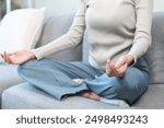 Meditation concept, closed eye asian young woman, girl hand in calm pose sitting practice meditating in lotus position on couch at home, relax, exercise for wellbeing. Relaxation, happy leisure people