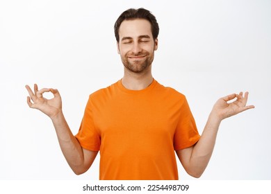 Meditation and mindfulness. Man meditating, practice yoga, reaching nirvana, feeling relaxed, standing in orange tshirt over white background - Shutterstock ID 2254498709