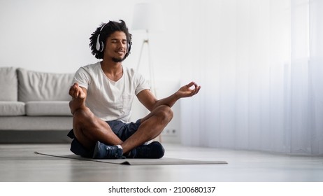 Meditation Practice. Relaxed Black Man Meditating At Home In Lotus Position, Smiling African American Guy Wearing Wireless Headphones Sitting With Closed Eyes On Yoga Mat, Panorama With Copy Space - Powered by Shutterstock