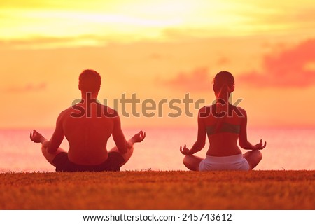 Meditation yoga couple meditating at serene beach sunset. Girl and man relaxing in lotus pose in calm zen moment in the ocean during yoga holiday class at resort retreat.