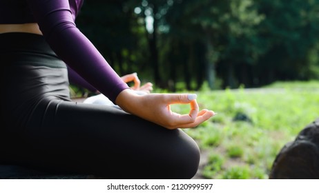 Meditation, yoga, spirituality, mindfulness concept. Close up young caucasian woman sitting in lotus position, sukhasana mudra asana outdoors on sunny day, side view. Selective focus on female hand.