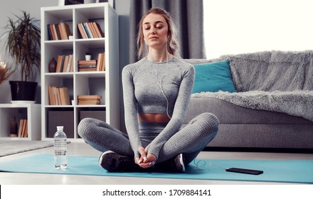 Meditative lady with closed eyes sitting with folded legs on exercise mat on floor listening to music - Shutterstock ID 1709884141