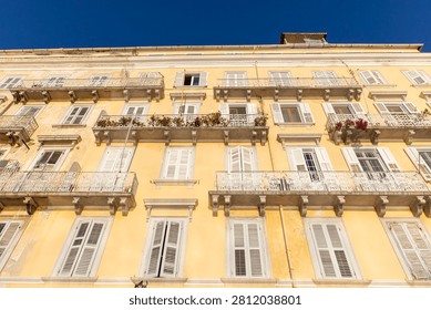 Mediterranean architecture featuring multiple windows, ornate balconies, and white shutters on a yellow building under a clear blue sky