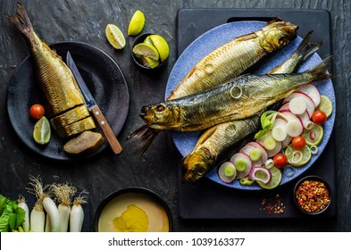Mediterranean food, smoked Herring fish served with green onion,lemon,cherry tomatoes,spices,bread and Tahini sauce on dark background.Top view with close-up