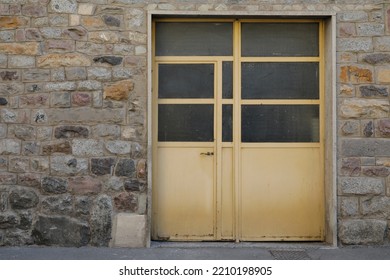 Mediterranean House Wall With Bricks And A Green Closed Metal Door With Glass Windows, Shadow On The Door, No Person