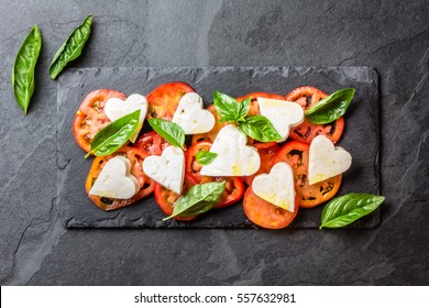 Mediterranean Italian Caprese Salad With Tomatoes And Cheese Mozzarella Cut As Hearts And Basil On Stone Slate Plate On Slate Background. Valentine Day Menu Consept. Healthy Food. Top View