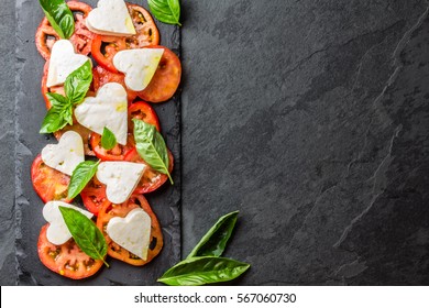 Mediterranean Italian Caprese Salad With Tomatoes And Cheese Mozzarella Cut As Hearts And Basil On Stone Slate Plate On Slate Background. Valentine Day Menu Consept. Healthy Food. Top View