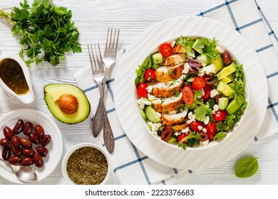 Mediterranean Rotisserie Chicken Salad With Avocado, Lettuce, Kalamata Olives, Cucumber, Tomato And Crumbled Feta Cheese With Vinaigrette Dressing In White Bowl On White Wood Table, Flat Lay, Close-up