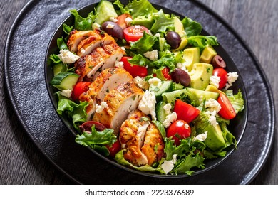 Mediterranean Rotisserie Chicken Salad With Avocado, Lettuce, Kalamata Olives, Cucumber, Tomato And Crumbled Feta Cheese In Black  Bowl On Dark Wood Table