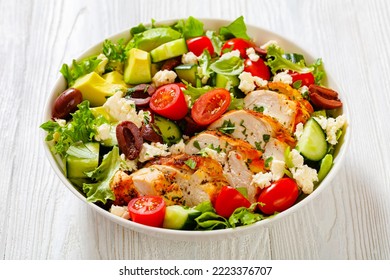 Mediterranean Rotisserie Chicken Salad With Avocado, Lettuce, Kalamata Olives, Cucumber, Tomato And Crumbled Feta Cheese In White Bowl On White Wood Table