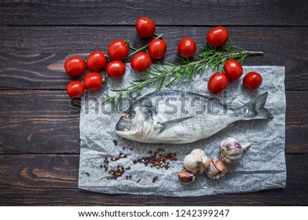 Mediterranean seafood concept. Raw dorado fish with garlic, tomatoes and rosemary on wooden table. Fresh organic sea bream or dorada fish. Top view, copy space