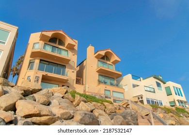 Mediterranean Style Buildings With Window Walls At Oceanside, California. Beachfront Houses Near The Seawall With Large Rocks And Handrails At The Front.