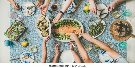 Mediterranean Style Dinner. Flat-lay Of Table With Cooked Salmon, Starters, Bread, Lemonade Over Blue Table Cloth With Hands Holding Drinks And Sharing Food, Top View. Holiday Party Concept